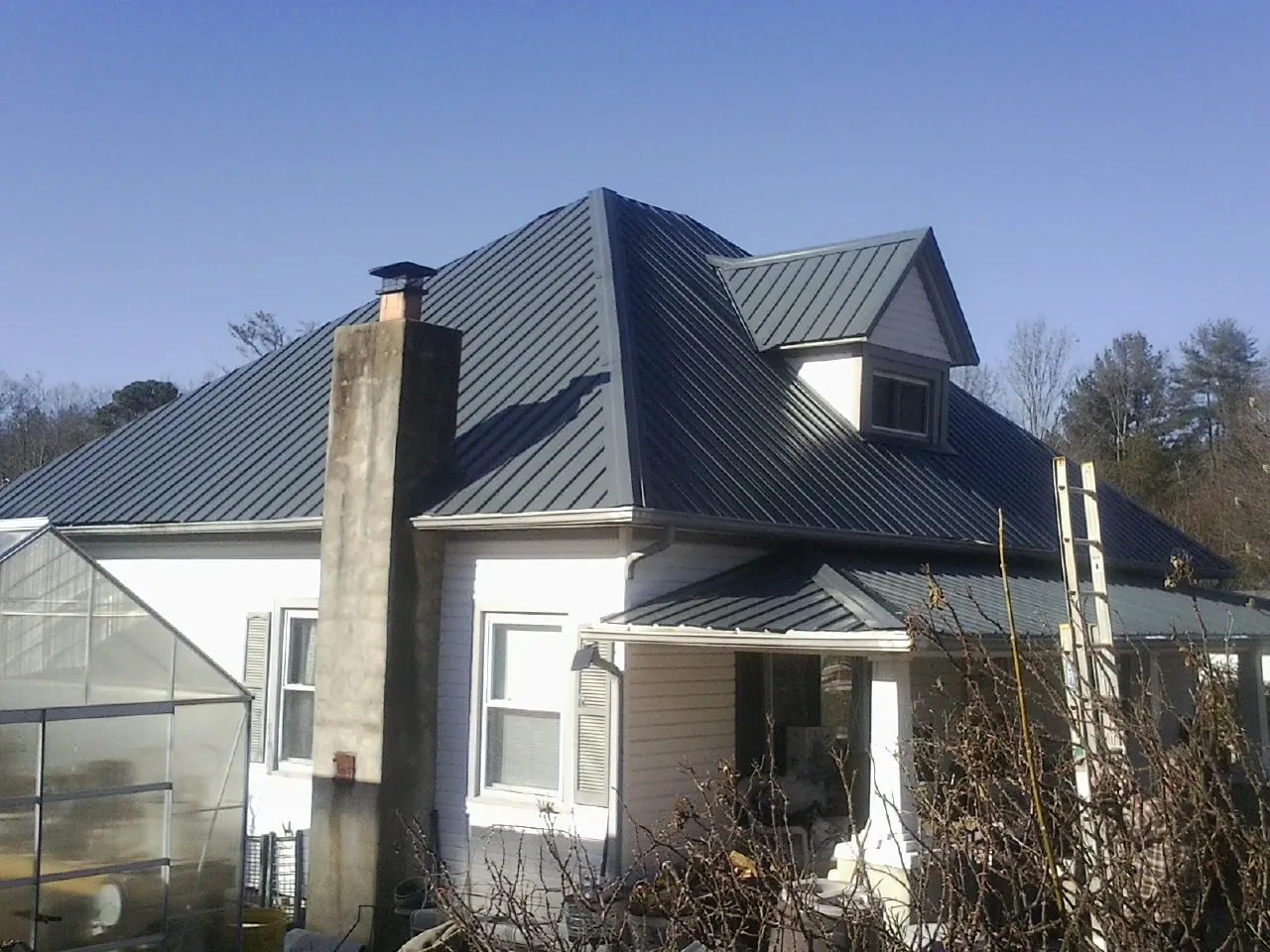 Dark blue standing seam metal roof on a white farmhouse with dormer — Slate & Tile Roof Repair by Roofing Brothers in Ashley