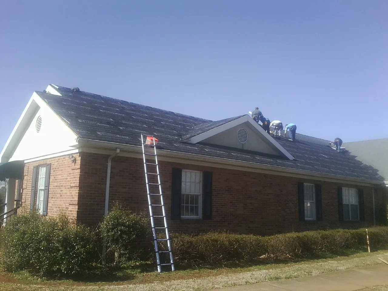 Crew tearing shingles off a brick ranch roof with a ladder set — Metal Roof Repair work by our crew in Ashley