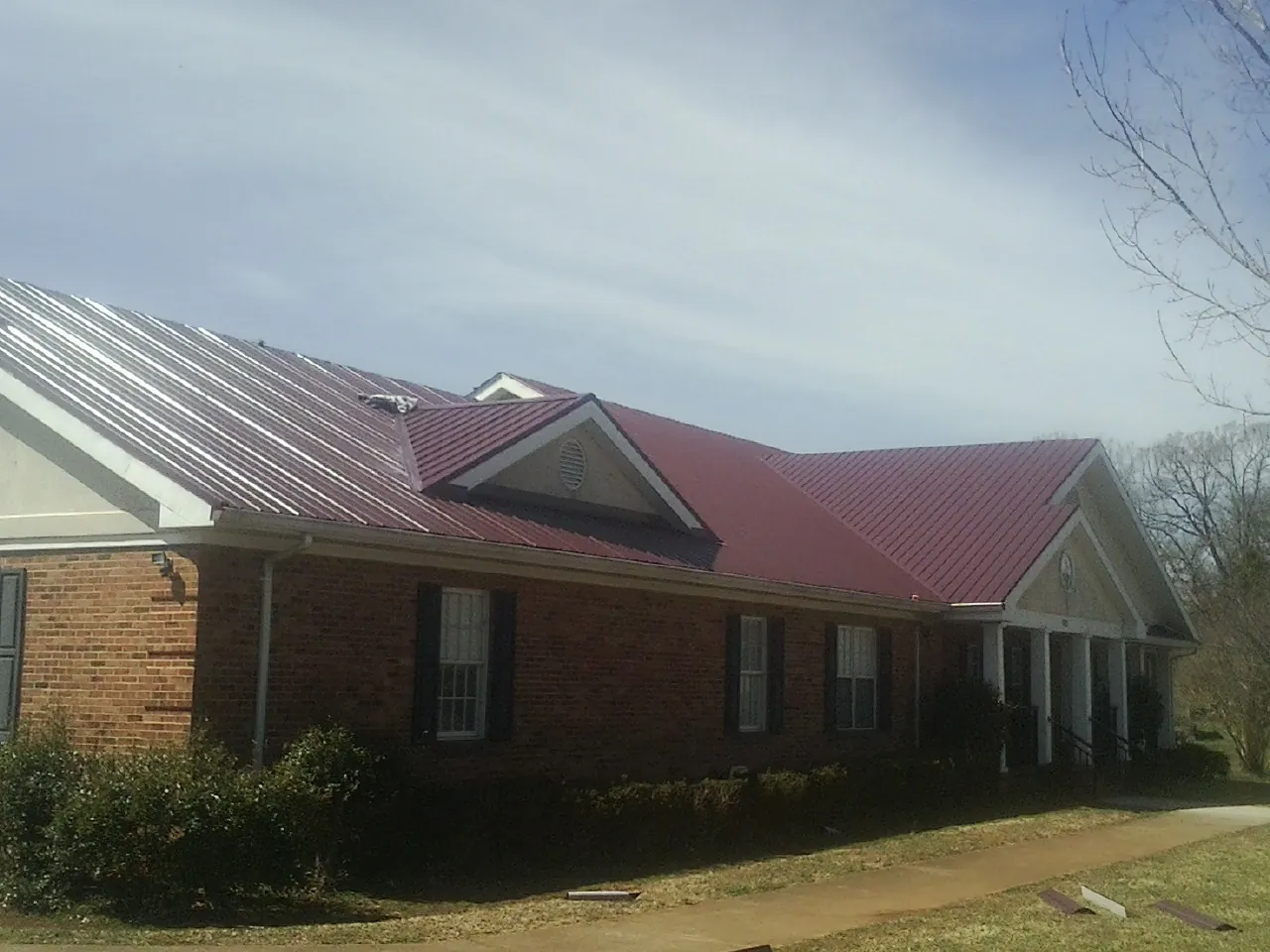 Red metal roof with gabled entries on a long brick building, from a Hail Damage Roof Repair job in Ashley
