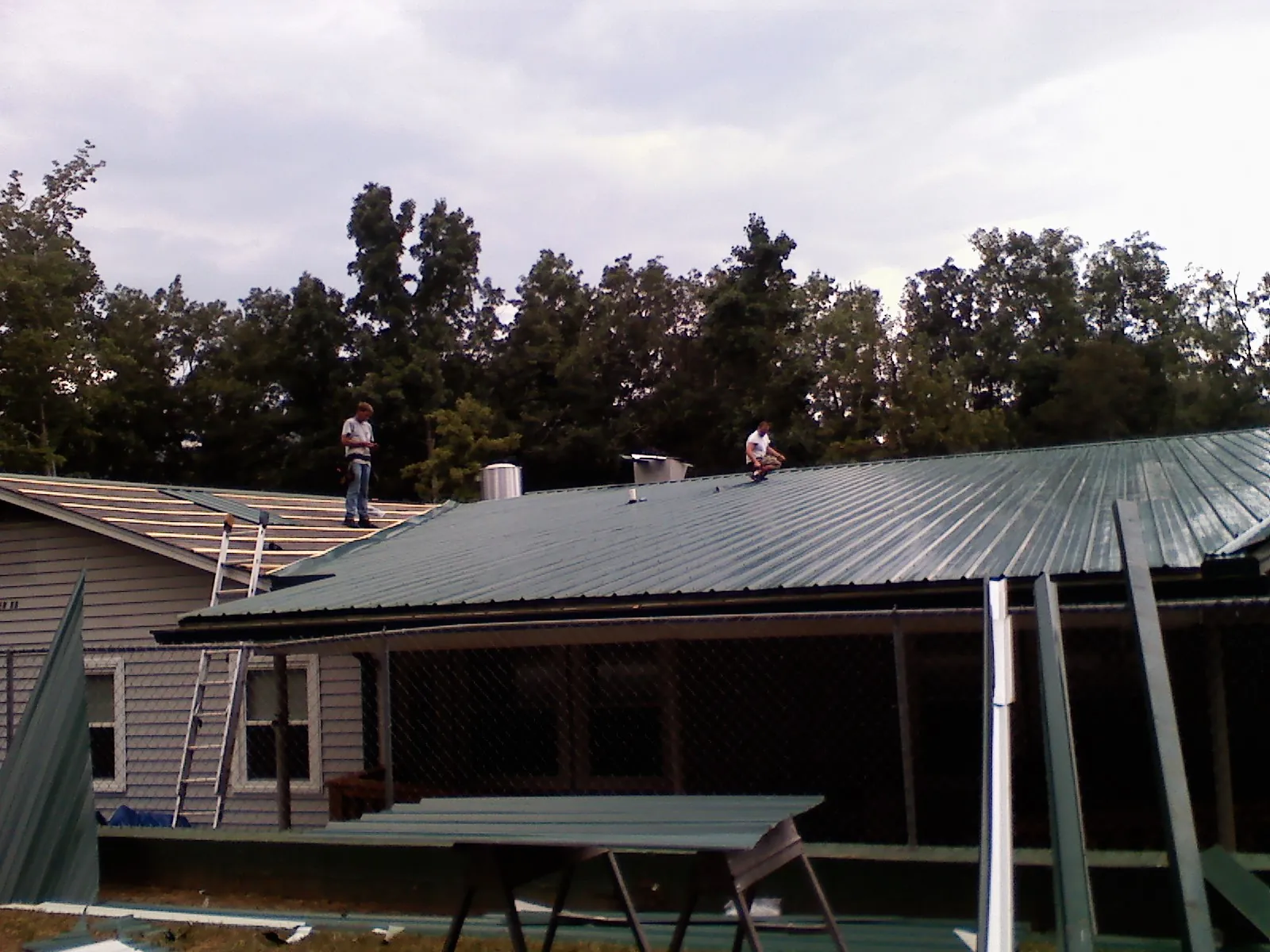 Two roofers installing green metal panels above a covered porch in Ashley